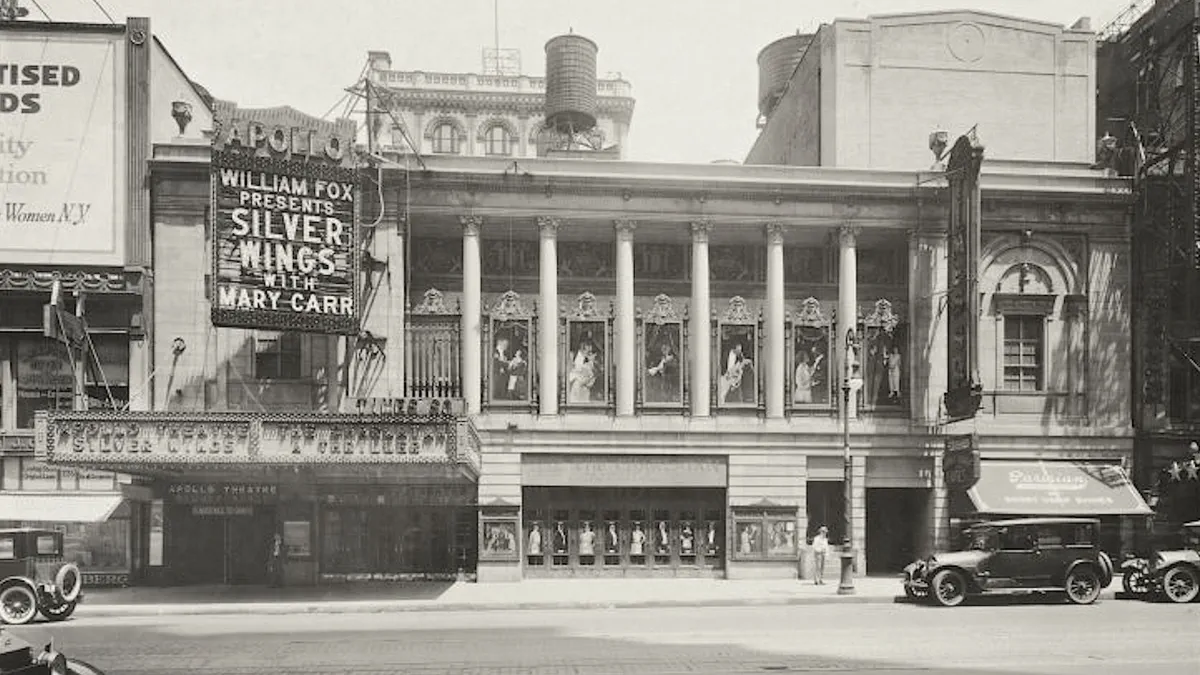 Two theatre facades on 42nd Street in 1922: a projecting marquee lettered Apollo, a hanging sign advertising a film, posters in the arched panels above the doors, and a car at the kerb.