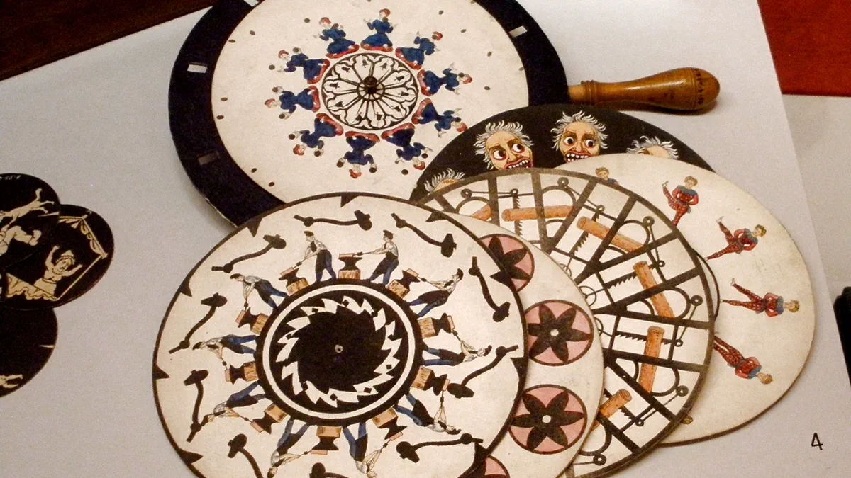 Several hand coloured card discs in a museum case, each painted with a ring of figures in slightly different positions: dancers, a man sawing, and rows of open mouths.
