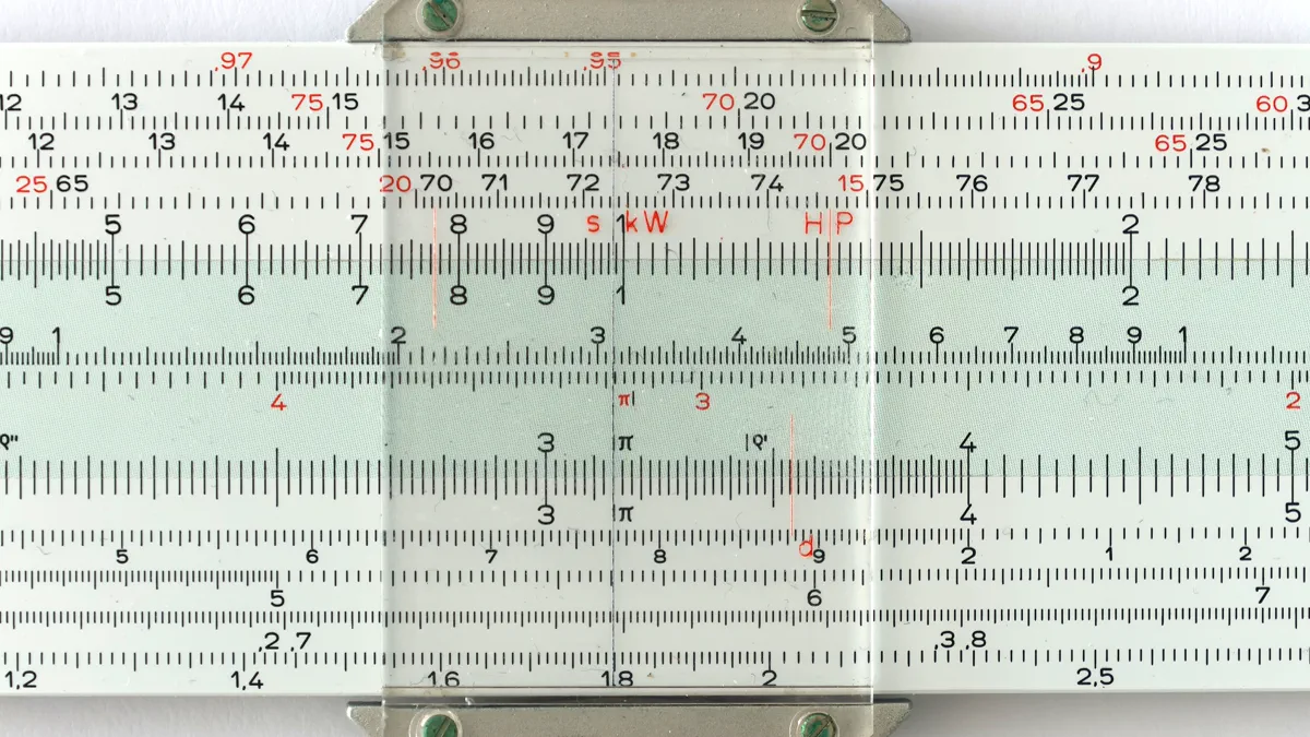 A close view of a slide rule: two printed scales sliding past each other under a clear plastic cursor, with red and black numbers and a fine index line.
